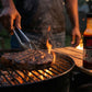 Person grilling steak with a bottle of steak sauce on a wooden board.